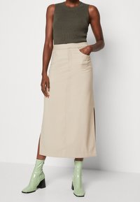 Beige midikjol med sidoklyftor, kombinerad med en mörkgrön ribbad tanktop och glänsande mintgröna ankelboots med fyrkantiga klackar.