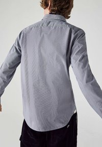 Vaaleanharmaa pitkähihainen paita, jossa on teksturoitu ruutukuosi. Siinä on klassinen kaulus ja kaareva helma.