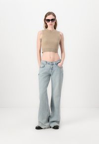 Top court côtelé beige, jeans large bleu clair, chaussures noires et lunettes de soleil sombres ; présente un design ajusté et une taille haute.