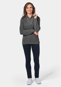 Grijze ribbelpullover met een kwart rits kraag, voorzien van lange mouwen en een relaxte pasvorm. G gedragen met donkere jeans en witte sneakers.