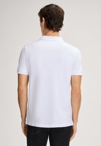 Witte poloshirt met korte mouwen, een klassieke kraag en een rechte zoom. Gemaakt van zachte katoen met een label aan de zijkant.