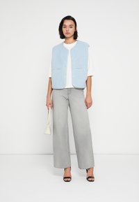 Φωτεινό γαλάζιο, υφασμάτινο γιλέκο με κουμπιά μπροστά, φορεμένο πάνω από άσπρο πουκάμισο. Συνδυασμένο με γκρίζο τζιν με φαρδιά μπατζάκια και μαύρα σανδάλια με ψηλό τακούνι.