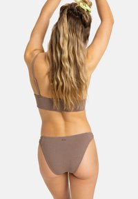 Brun bikiniuppsättning med texturerad yta, tunna remmar och minimal bakdesign som visar en sömlös stil.