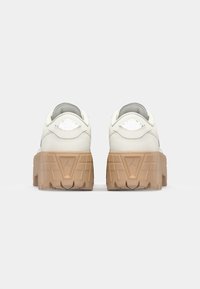 Hvide lædersneakers med en tykk tan gummisål, der har et forhøjet logo på hælen og en glat, tekstureret overdel.