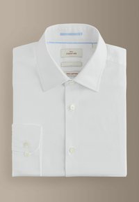 Bela bombažna srajca z dolgo rokavi, značilna klasična ovratnica, gumbi, levi žep ter etikete, ki označujejo 100 % bombaž in podpis blagovne znamke.