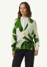 Groene en witte cardigan met een tropisch bladerenpatroon, voorzien van een enkele knoopsluiting en ribgebreide manchetten, gecombineerd met een wit shirt.