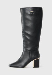 Stivale in pelle nera al ginocchio con punta a punta, tacco a blocco con rifiniture dorate e piccolo logo DKNY vicino alla parte superiore.