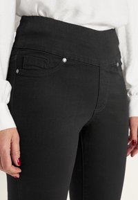 Svarta högmidjade jeans i denim med en slät textur, frampockets och silverfärgade knappdetaljer på midjebandet.