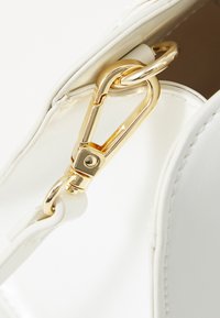 White faux leather bag with a gold metal clip and ring, featuring a smooth surface and clean stitching details along the edges.