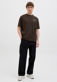 Brown short-sleeve T-shirt with a crew neck and white text detail, paired with loose black pants and gray sneakers.