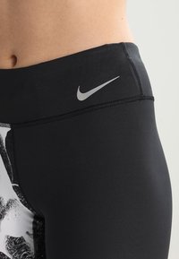 Collant sportivi neri con un design stampato, dotati di un logo Nike argentato sulla vita. Texture liscia con una vestibilità aderente e a vita alta.