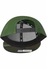 Grüne Kappe mit einem schwarzen Schirm, der ein Camouflage-Muster auf der Unterseite hat. Verstellbarer Riemen hinten, mit Mesh-Futter für Atmungsaktivität.