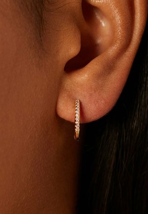 Gold hoop earring with a smooth finish, featuring a row of small, clear gemstones on one side, worn on the lobe of an ear.