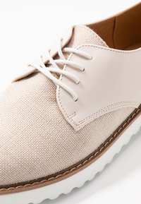 Scarpa beige chiaro lace-up con tomaia in tessuto testurizzato, dettagli in pelle liscia e una spessa suola in gomma bianca. Dettaglio di cuciture in contrasto marrone.