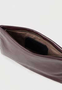 Κόκκινη δερμάτινη τσάντα χειρός με κλείσιμο φερμουάρ, που διαθέτει λεία υφή και απλό σχέδιο. Στο εσωτερικό υπάρχει καφέ επένδυση και μαύρος θήκη για κάρτες.