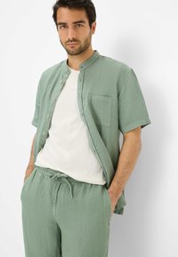 Light green short-sleeve shirt with a round collar and front buttons, paired with matching lightweight pants and a white t-shirt underneath.
