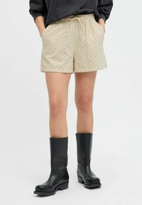 Cremfarbene Shorts mit gesticktem Punkte-Muster, elastischem Bund, Kordelzug und Seitentaschen, kombiniert mit schwarzen kniehohen Stiefeln.