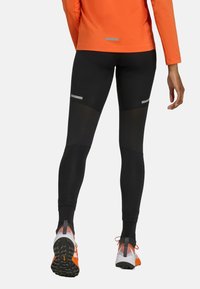 Svarta träningsleggings med mesh-paneler, reflexdetaljer och en åtsittande design. Matchas med orangea och grå träningsskor.