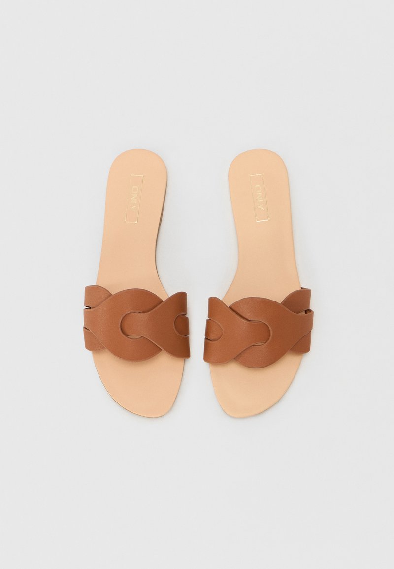 Sandales en cuir marron avec un large design de bride entrelacée, semelle plate et semelle intérieure beige lisse, présentant des accents minimalistes.