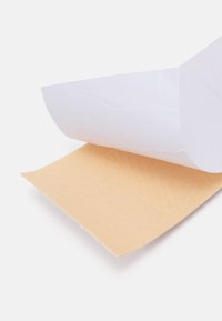 Delvist uafviklet beige klæbende stofpatch med hvidt beskyttelseslag papir på en hvid overflade.