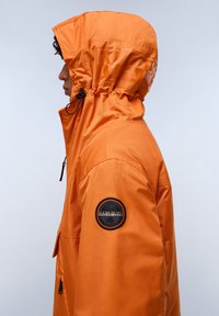 Orange waterproof jacket with a hood, featuring a black logo patch on the sleeve, and a smooth, shiny texture. Adjustable drawstring on the hood.