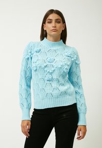 Maglione lavorato a maglia blu chiaro con colletto alto, motivi floreali intricati e texture, e polsini e orlo a coste.