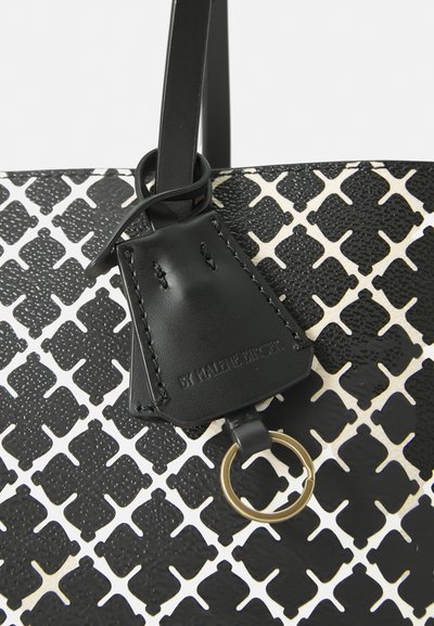Black and white tote bag with a textured pattern, featuring a black leather tag and gold ring hardware. Smooth material with contrasting accents.