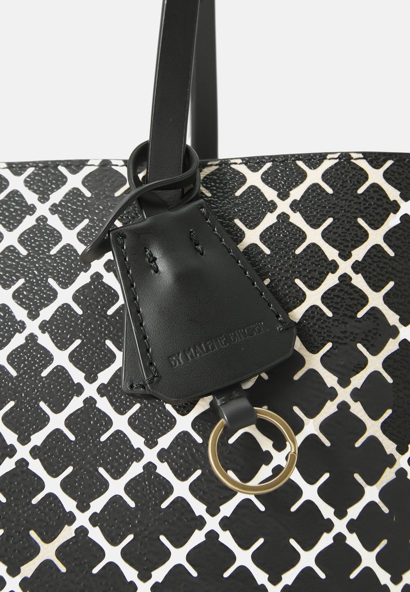 Svart och vit tygväska med en texturerad mönstring, med en svart läderlapp och guldringsbeslag. Slätt material med kontrasterande accenter.