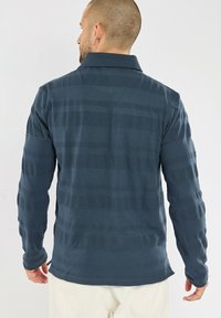 Polo à manches longues bleu marine avec un motif texturé. Présente un col et un ourlet droit, offrant une coupe décontractée.