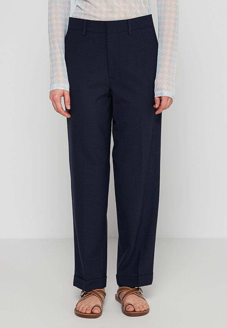 Marineblaue, taillierte Hose mit geradem Schnitt, ausgestattet mit einem cleanen Taillenbund, seitlichen Taschen und einem umgeschlagenen Saum. Der Stoff wirkt glatt und strukturiert.