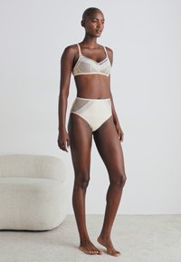 Beige lingerie set featuring a bralette with geometric mesh panels and high-waisted bottoms. Soft texture and elastic straps.