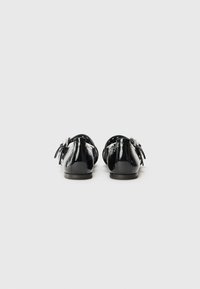 Black patent leather flats with bow detail at the back. Features smooth texture and a rounded toe, set on a low-profile sole.