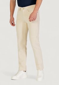 Pantaloni beige chiaro con una finitura testurizzata, dotati di tasche frontali e chiusura con bottone, abbinati a sneaker bianche.