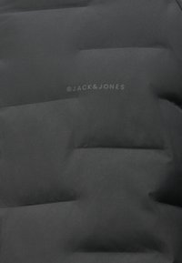 Zwarte pufferjack met gequiltte delen, een soepele textuur en een subtiele bedrukte logo "© JACK & JONES" op de onderkant.