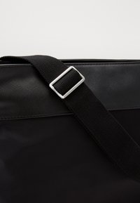 Borsa a tracolla nera con una superficie liscia e lucida, dotata di una robusta tracolla in tessuto e una elegante fibbia in metallo argentato.