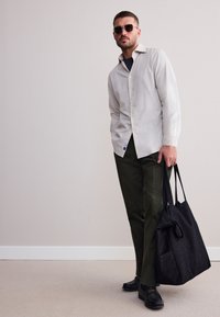 Chemise boutonnée gris clair, pantalon vert olive, sac fourre-tout noir et lunettes de soleil ; tissu lisse, coupe ajustée et design minimaliste.
