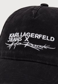 Fekete farmer sapka fehér hímzett "KARL LAGERFELD JEANS X" logóval és aláírás részlettel. Strukturált dizájn, ívelt vízvonallal.