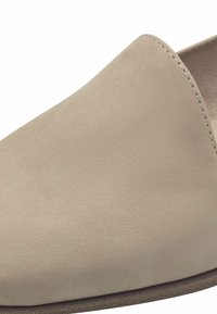 Beige slip-on sko laget av glatt skinn, med en rund tå og minimalt med sømmer, med en noe teksturert overflate.