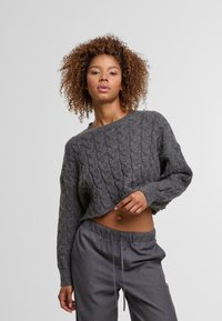 Harmaa neulepaita, jossa on köysikuvio, lyhyt malli ja pitkät hihat, yhdistettynä löysiin harmaisiin housuihin, joissa on elastinen vyötärö.