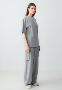 Graues, Rundhals-T-Shirt mit kurzen Ärmeln, kombiniert mit weiten grauen Hosen mit großen Seitentaschen. Weicher Stoff.