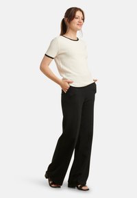 Witte gebreide top met textuur en zwarte bies, gecombineerd met hoge taille zwarte wijde broek en zwarte sandalen met een blokhak.