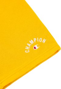 Gelbes Baumwoll-T-Shirt mit Rundhalsausschnitt; verfügt über das weiße, gestickte "CHAMPION"-Logo und ein rundes Emblem. Weiche Textur und kurze Ärmel.