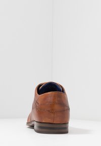 Chaussure en cuir marron avec une texture lisse, bout arrondi et couture décorative. Talon bas avec un accent en bois foncé contrasté.