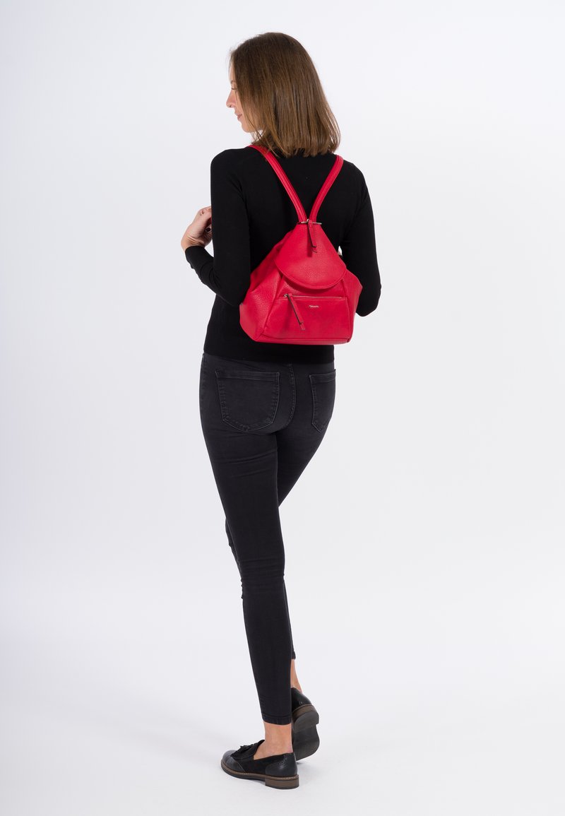 Zaino in pelle rossa con coulisse, dalla texture liscia, una tasca frontale con zip e due spallacci regolabili, indossato sulla schiena di una persona.