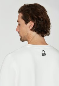 Sudadera blanca con cuello redondeado, que presenta un gráfico de aguacate negro en la parte posterior. La tela parece suave con una textura lisa.
