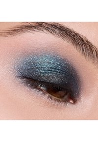 Close-up of an eye featuring shimmery blue and black eyeshadow with a soft gradient effect; fine glitter particles visible on the eyelid.