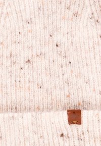 Dzianinowa czapka w jasnym kremie z flekami brązu i pomarańczy. Posiada małą brązową skórzaną metkę z logo. Miękka w dotyku.