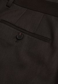 Ciemnobrązowe dopasowane spodnie wykonane z teksturowanej tkaniny, z zapięciem na guzik i jedną tylną kieszenią z wąskim wykończeniem.