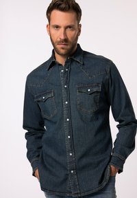 Donkere spijkerblouse met lange mouwen, knoopsluiting aan de voorkant, twee borstzakken en contrasterende stiksels. Heeft een ontwerp met een western-stijl yoke.