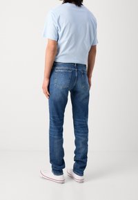 Camiseta de manga corta azul claro combinada con jeans de mezclilla de lavado medio. Los jeans tienen un corte recto y bolsillos traseros estándar, usados con zapatillas blancas.